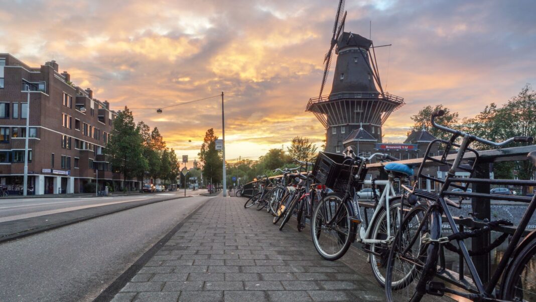 Rzędy rowerów przy ulicy i wiatrak w Amsterdamie o zachodzie słońca Rzędy rowerów przy ulicy i wiatrak w Amsterdamie o zachodzie słońca