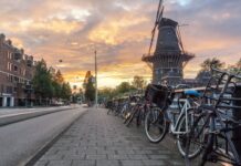 Rowery, wiatraki i bezkresne łąki: jak odkrywać Holandię aktywnie Rzędy rowerów przy ulicy i wiatrak w Amsterdamie o zachodzie słońca