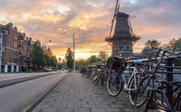 Rowery, wiatraki i bezkresne łąki: jak odkrywać Holandię aktywnie Rzędy rowerów przy ulicy i wiatrak w Amsterdamie o zachodzie słońca