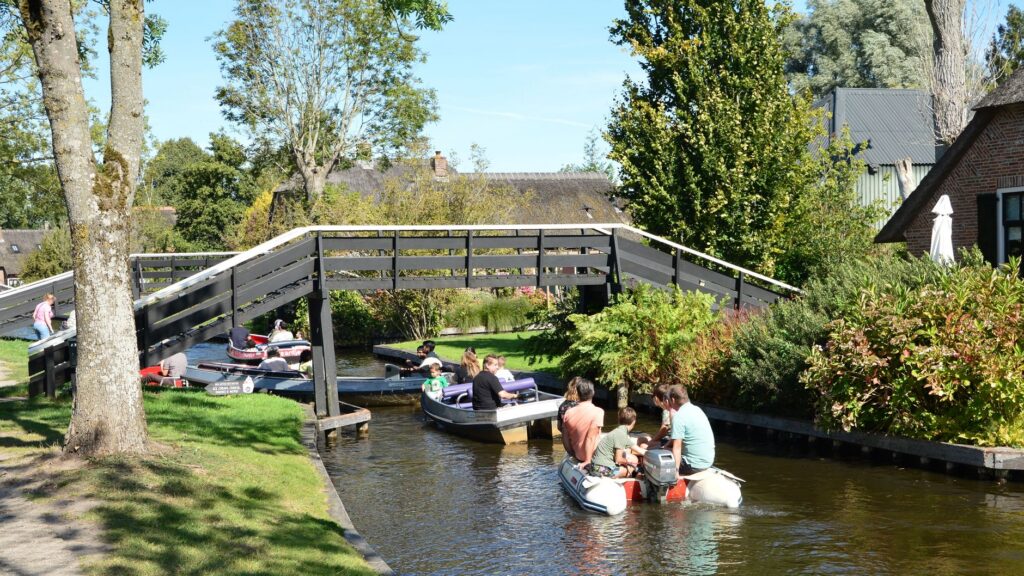 Rodziny płyną łodziami kanałem pod drewnianym mostem w Giethoorn